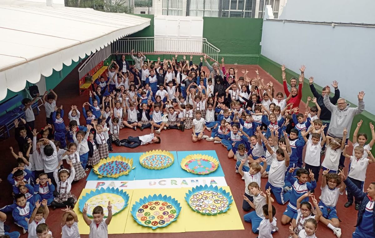 Grupo grande de
niños y maestros del Colegio Marpe sentados en el patio, formando un círculo alrededor
de pancartas que promueven la paz, celebrando un evento escolar